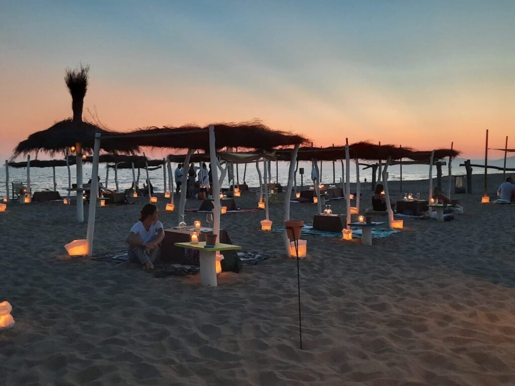Atmosfera romantica al tramonto sulla spiaggia di Kite Beach Fiumara, con lanterne e lettini accoglienti.